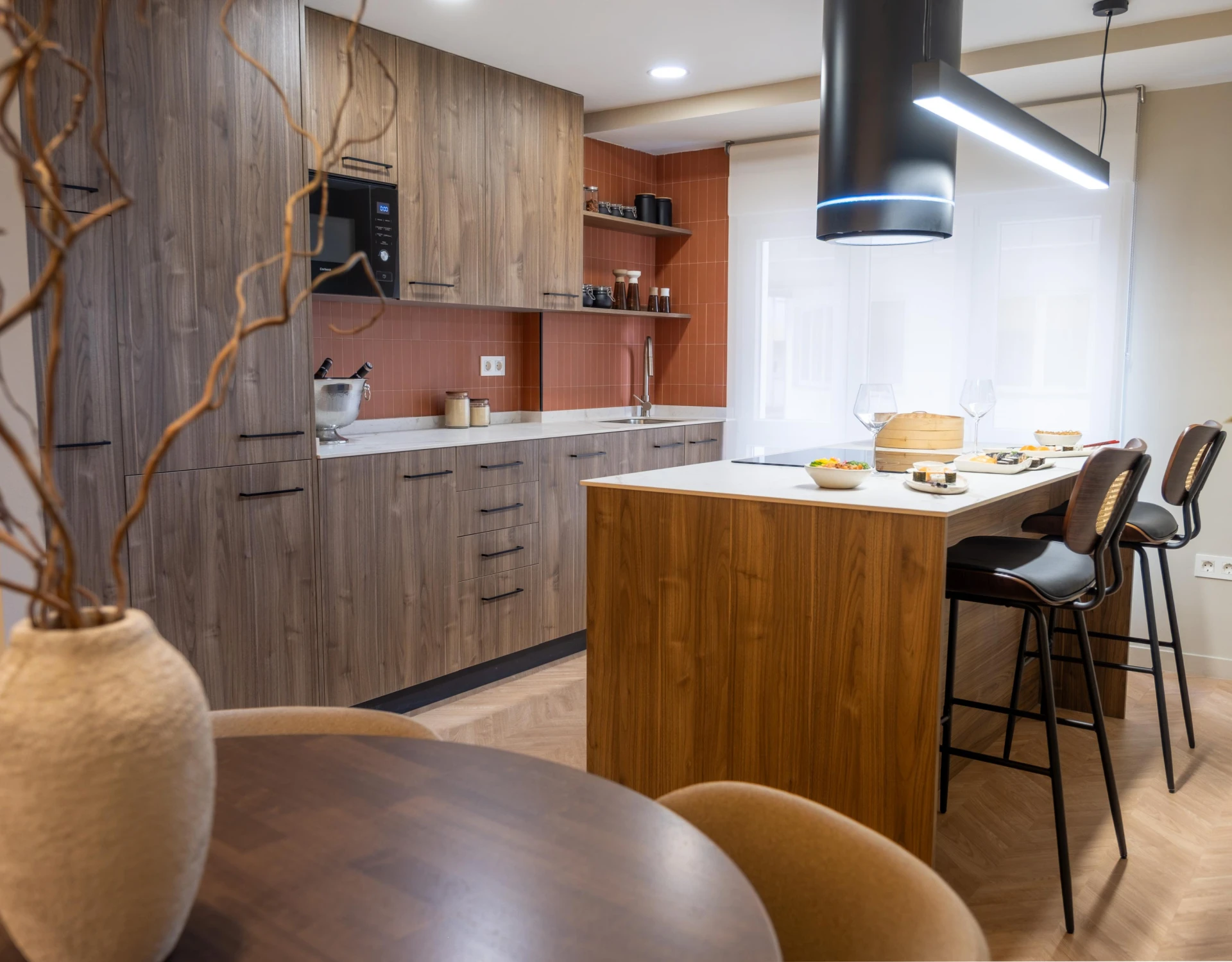 Interior de Casa 7G con cocina abierta, isla central, mobiliario en madera y lámpara suspendida