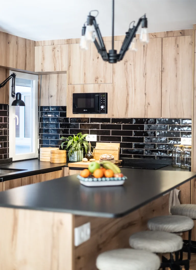 Interior de Casa M3 con cocina en madera, isla central y salpicadero de azulejo negro brillante