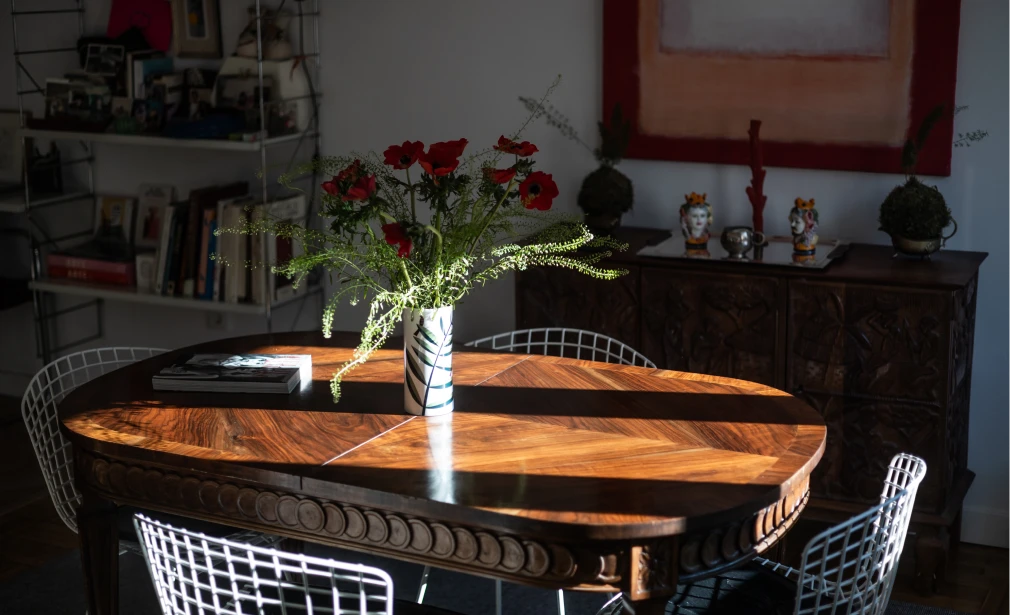 Comedor de Casa M3 con mesa de madera oscura, sillas metálicas blancas, flores y luz natural entrando en el espacio