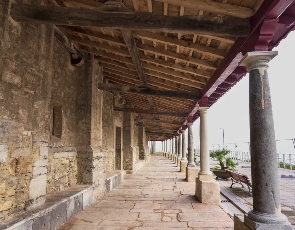 Vista interior del pórtico rehabilitado de Santa María de Luanco con columnas de piedra, estructura de madera y pavimento tradicional