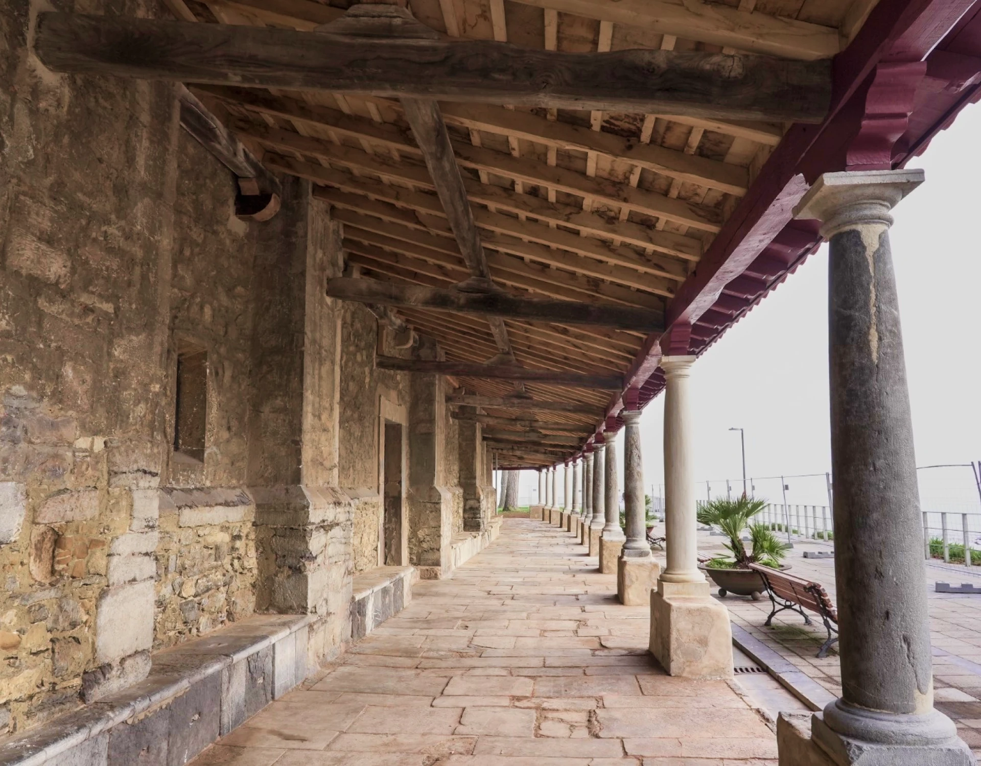 Vista interior del pórtico rehabilitado de Santa María de Luanco con columnas de piedra, estructura de madera y pavimento tradicional